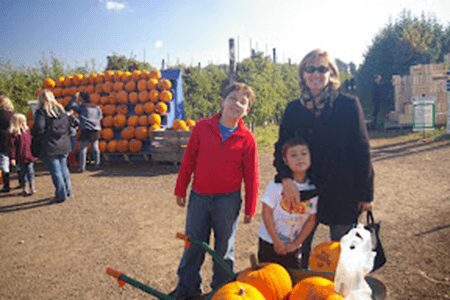 A woman and two children stand in front of pumpkins.