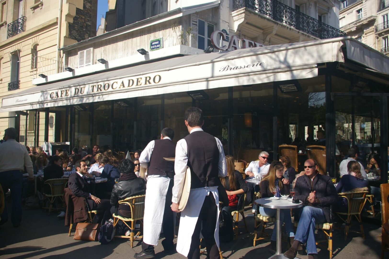 A group of people sitting at tables outside of a restaurant.