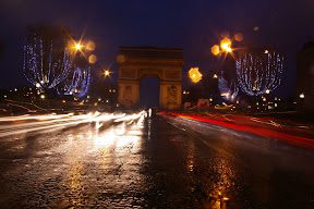 A street with lights and a large arch in the background.