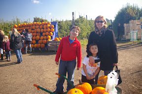 A woman and two children stand in front of pumpkins.