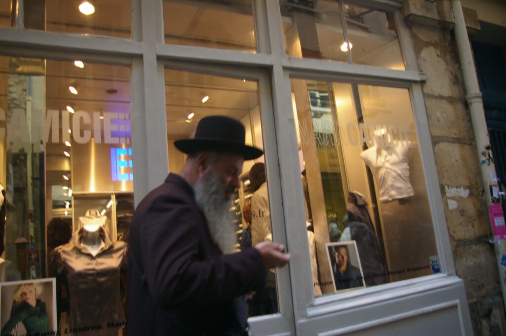 A man in a hat and beard standing outside of a store.