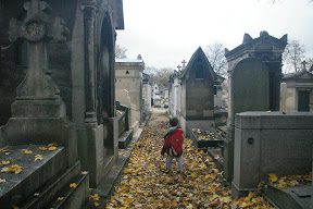 A child is walking through the leaves in an old cemetery.