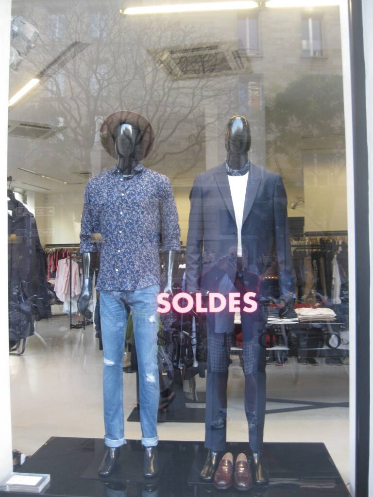 Two mannequins in a store window with the sign " soldes ".