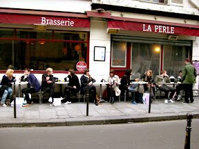 A group of people sitting at tables outside of a restaurant.