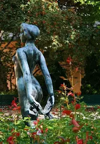 A statue of a naked man in the middle of a garden.